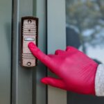 Visitor pressing a modern doorbell on a front door, illustrating the rumored Apple Face ID video doorbell