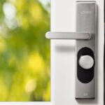 Sleek smart door lock on a white front door with green foliage in the background