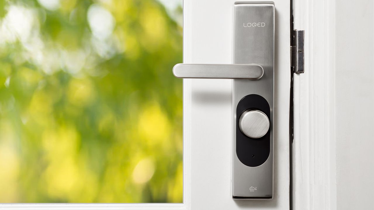 Sleek smart door lock on a white front door with green foliage in the background